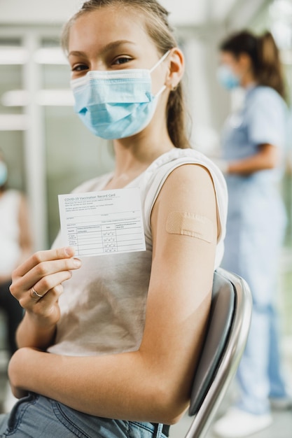 Een schattig tienermeisje met een glimlach die het vaccinatiecertificaat laat zien na ontvangst van het Covid-19-vaccin.