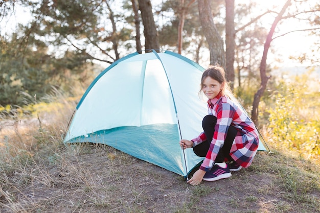 Een schattig tienermeisje zet een tent op in het midden van een dennenbos Het concept van actief recreatief reizen in de zomer en avontuurlijk kamperen