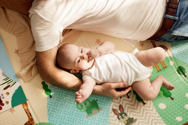 Een schattig vrolijk kind en zijn vader in een wit t-shirt en spijkerbroek liggen op de vloer in een lichte kamer en p