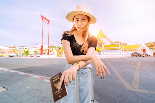 Een schattige Aziatische vrouw staat midden in de toeristische attracties van Bangkok in Thailand Met een koffer en paspoort De achtergrond is Giant Swing
