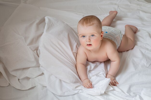 Een schattige baby ligt in luiers in een bed met wit katoenen beddengoed. hoge kwaliteit foto