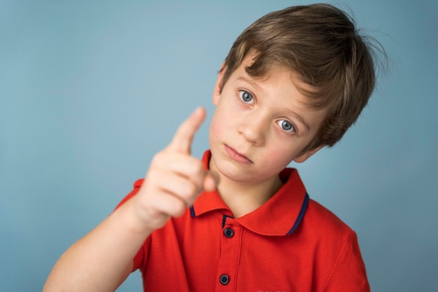 Een schattige blanke jongen van 5 jaar oud in een rood T-shirt schudt bedachtzaam, serieus en stichtelijk zijn vinger. Blauwe achtergrond. kopieer ruimte