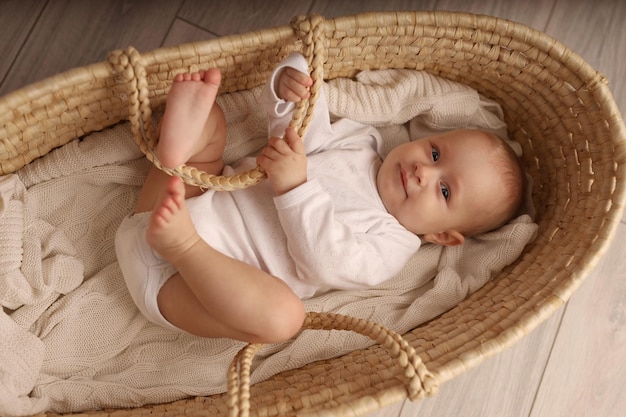 een schattige blondharige baby in een wit pak ligt in een strogeweven wieg