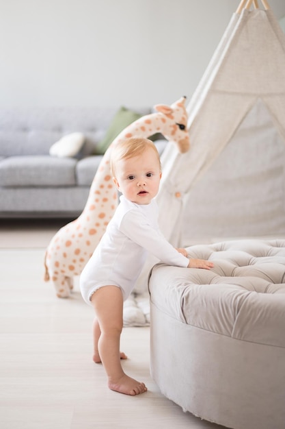 Een schattige gezonde babyjongen in een ruime lichte kinderkamer thuis met een wigwam zacht speelgoed kindertextiel Het kind zelf staat met steun