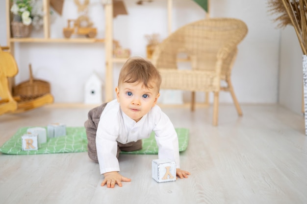 Een schattige gezonde babyjongen speelt met houten educatief speelgoed in een lichte, gezellige kinderkamer thuis tegen de achtergrond van een houten huis