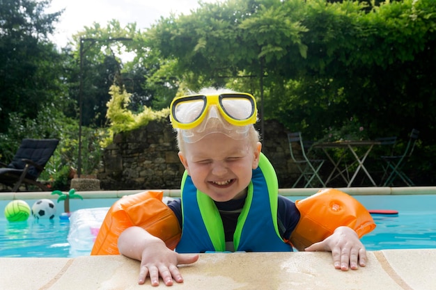 Een schattige jonge jongen met armbanden en een veiligheidsbril die plezier heeft in een zwembad op vakantie