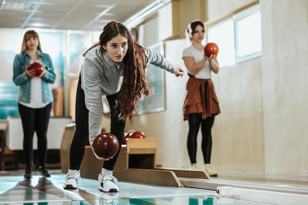 Een schattige jonge vrouw gooit de bowlingbal terwijl haar vrienden achterin staan.