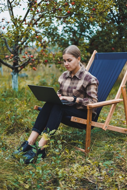Een schattige jonge vrouwelijke freelancer werkt buiten in de tuin terwijl ze in een comfortabele tuinstoel zit Werk op afstand op een draagbare laptop