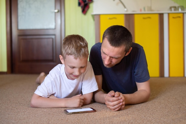 Een schattige jongen ligt bij zijn vader en kijkt naar de telefoon