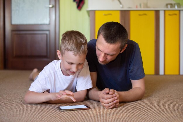 Een schattige jongen ligt bij zijn vader en kijkt naar de telefoon