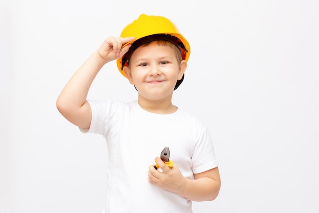 Een schattige jongen met een helm kijkt naar rechts, in de handen van een kind met een moersleutel en een hamer. Het concept van het belang van het gebruik van persoonlijke beschermingsmiddelen en speciaal gereedschap