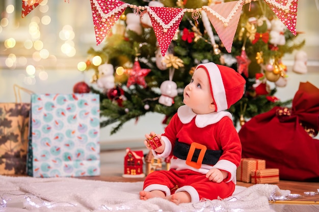 Een schattige jongen verkleed als de kerstman speelt in de buurt van een versierde kerstboom in de woonkamer.