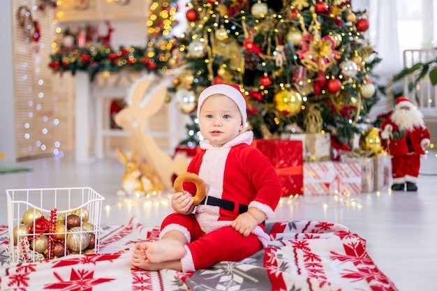 Een schattige kleine babyjongen in een kerstmankostuum zit met kerstboomspeelgoed