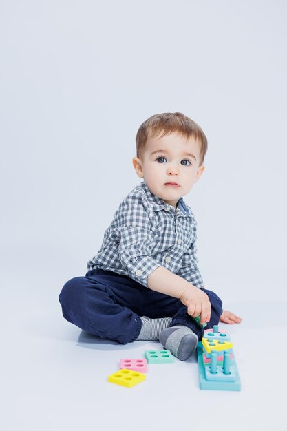 Een schattige kleine jongen in een geruit overhemd zit op een witte achtergrond en speelt met houten educatief speelgoed Ecologisch houten speelgoed voor kinderen