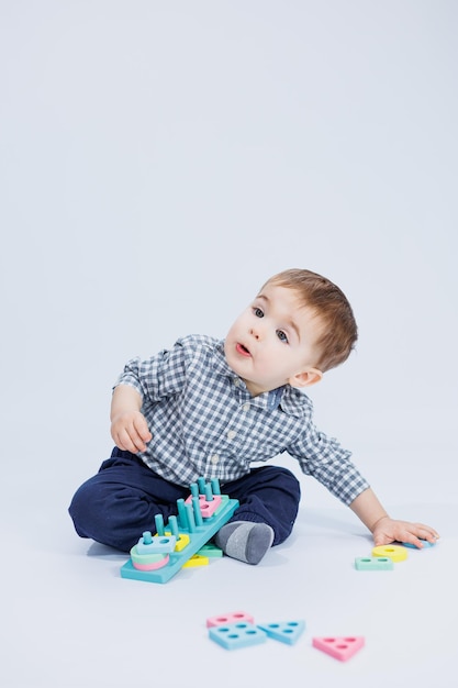 Een schattige kleine jongen in een geruit overhemd zit op een witte achtergrond en speelt met houten educatief speelgoed Ecologisch houten speelgoed voor kinderen