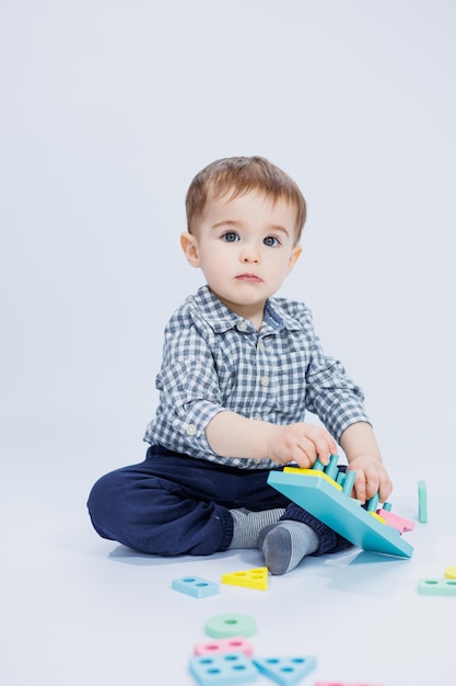 Een schattige kleine jongen in een geruit overhemd zit op een witte achtergrond en speelt met houten educatief speelgoed Ecologisch houten speelgoed voor kinderen