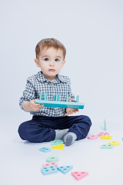 Een schattige kleine jongen in een geruit overhemd zit op een witte achtergrond en speelt met houten educatief speelgoed Ecologisch houten speelgoed voor kinderen