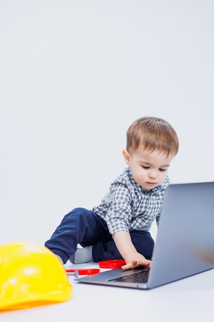 Een schattige kleine jongen in een geruit overhemd zit op een witte achtergrond met een laptop Kinderspeelgoed