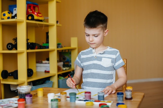 Een schattige kleine jongen is aan het spelen en schilderen in zijn kamer. Recreatie en amusement. Blijf thuis.