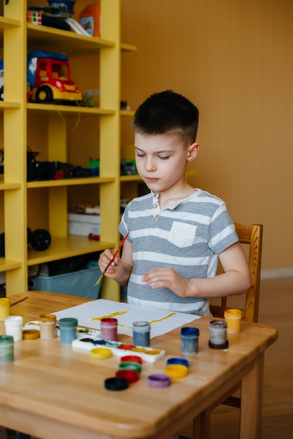 Een schattige kleine jongen speelt en schildert in zijn kamer. Recreatie en amusement. Blijf thuis.