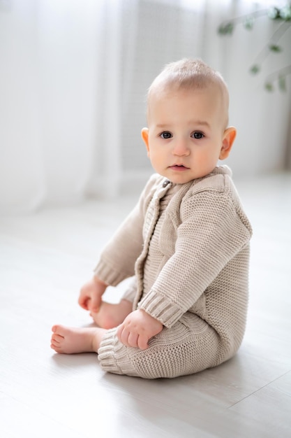 Een schattige kleine jongen zit op de grond en leert een groot portret van een kind met bruine ogen en blond haar in een gebreid pastelkleurenpak te zitten