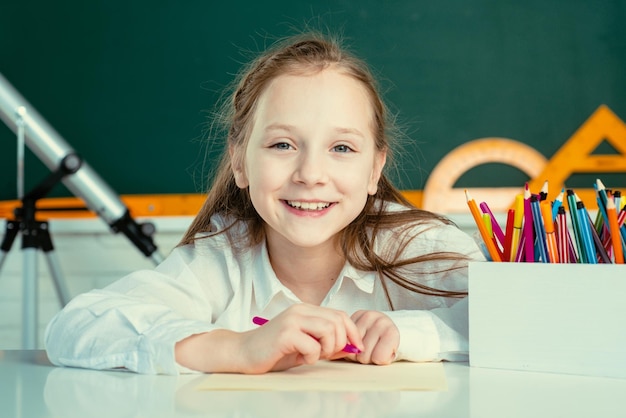 Een schattige kleine schooljongen die een huis tekent en naar een camera kijkt, tekent een schattig kind met kleurrijke krijtjes a