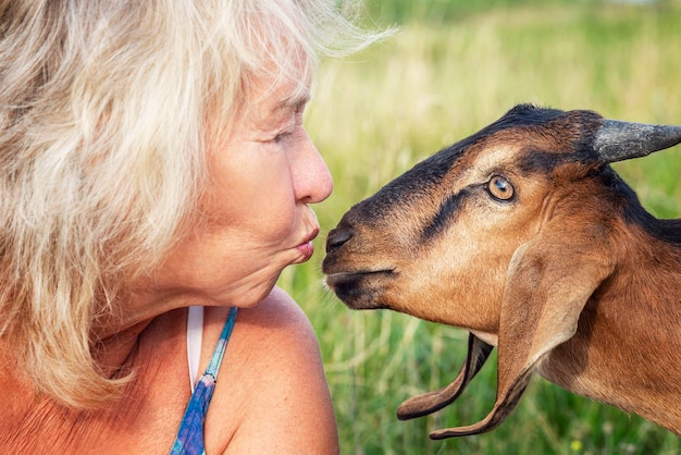Foto een schattige oudere vrouw kust een geit in een veld op een zomerdag liefde en tederheid voor dieren close-up