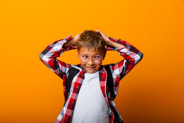 Een schattige schooljongen in een geruit overhemd houdt zijn hoofd vast met zijn handen. isolatie op een gele achtergrond.