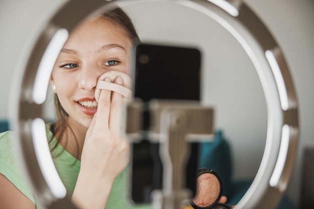 Een schattige tienermeisje vlogger die live-uitzendingen make-up tutorial voor haar volgers via smartphone bij haar thuis.