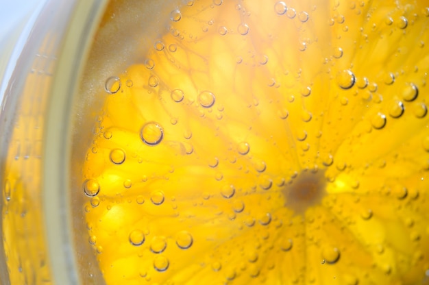 Een schijfje sinaasappel bedekt met bubbels ligt in een glas bruisend water. Detailopname.