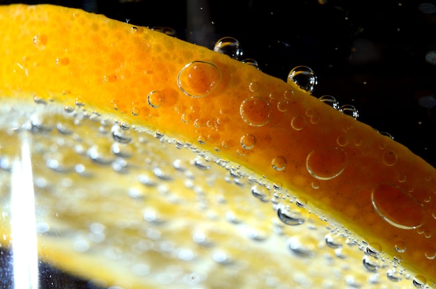 Een schijfje sinaasappel bedekt met bubbels ligt in een glas bruisend water. Detailopname.