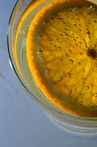 Een schijfje sinaasappel bedekt met bubbels ligt in een glas bruisend water. Detailopname.
