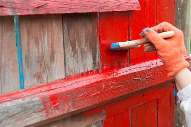 Een schilder die met de hand een houten hek schildert met rode kleur