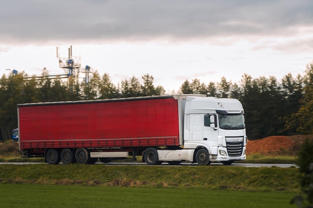 Een schilderachtige route wordt een achtergrond voor een rode vrachtwagen die een lading levert op een weg een weerspiegeling van de logistieke keten en de wereldwijde scheepvaart die de wereld verbindt