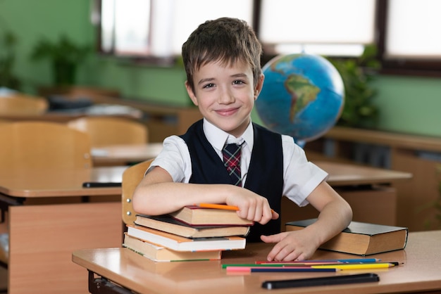 Een schooljongen zit aan een bureau in een leeg klaslokaal en schrijft iets in een notitieboekje