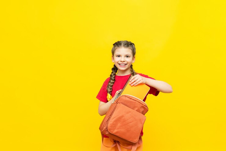 Een schoolmeisje bereidt een tas voor school voor Een klein meisje verzamelt notitieboekjes en schoolboeken voor de schooldag op een gele geïsoleerde achtergrond Voorbereiding op examens