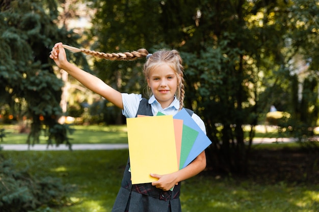 Een schoolmeisje gaat naar school met opgeheven handen op de achtergrond van het park. meisje in schooluniform in het park.