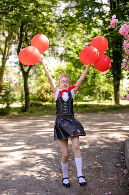 Een schoolmeisje in een witte blouse met een rode stropdas, met een strik en rode ballonnen in de klas. terug naar school-concept.