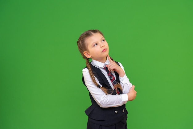 Een schoolmeisje kijkt bedachtzaam op een groene geïsoleerde achtergrond kopieerruimte schoolstudies en onderwijs