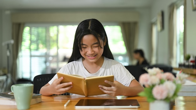 Een schoolmeisje leest een boek aan een houten bureau