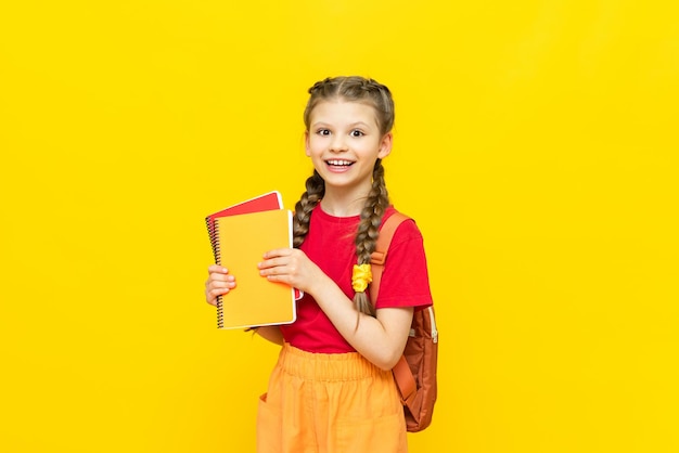 Een schoolmeisje met een rugzak en schriften bereidt zich voor op aanvullende trainingen Een mooi klein meisje gaat naar school op een gele geïsoleerde achtergrond