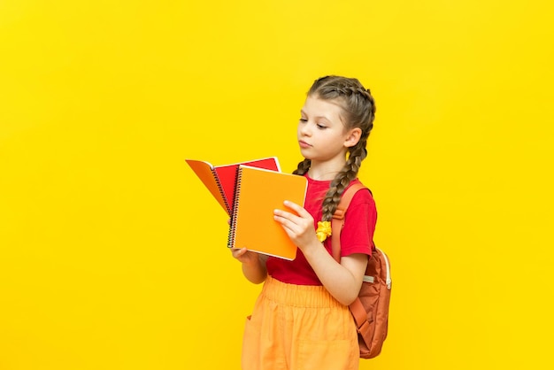 Een schoolmeisje met een rugzak en schriften bereidt zich voor op aanvullende trainingen Een mooi klein meisje gaat naar school op een gele geïsoleerde achtergrond