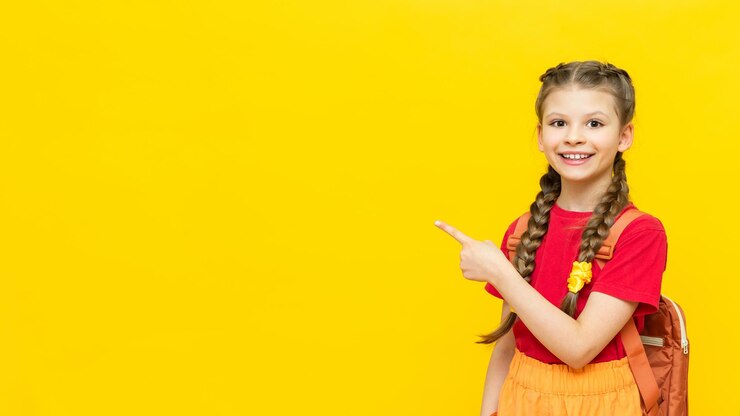 Een schoolmeisje wijst naar uw advertentie op een gele geïsoleerde achtergrond Aanvullende trainingen voor schoolkinderen Een vrolijk klein meisje wijst naar de advertentie