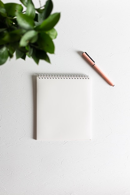 Een schoon wit spiraalvormig notitieboekje ligt op een witte structurele achtergrond. Ernaast staat een roze pen
