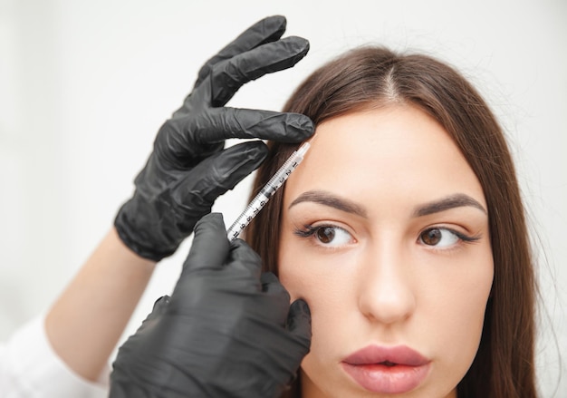 Een schoonheidsspecialist maakt anti-aging injecties tegen rimpels op het voorhoofd op het gezicht van een mooie vrouw Esthetische cosmetologie voor vrouwen in een schoonheidssalon