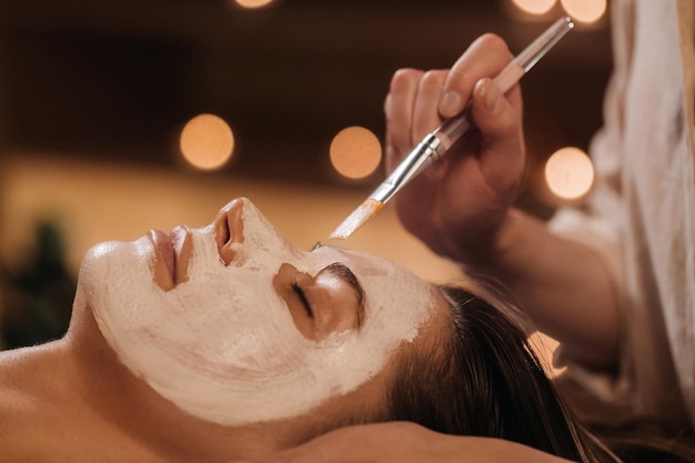 Een schoonheidsspecialist maakt een masker voor het gezicht van een vrouw om de huid te verjongen Cosmetologie