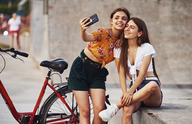 Een selfie maken. Twee jonge vrouwen met fiets hebben een goede tijd in het park.