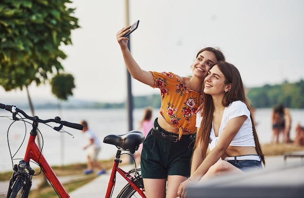 Een selfie maken. Twee jonge vrouwen met fiets hebben een goede tijd in het park.