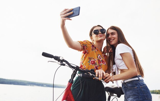 Een selfie maken. Twee vriendinnen op de fiets hebben plezier op het strand bij het meer.