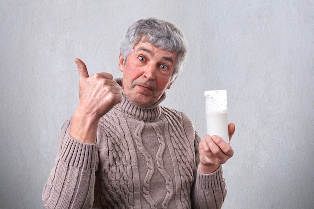 Een senior knappe man met een aangename uitstraling met een glas melk in zijn hand en laat met zijn duim zien dat hij het lekker vindt